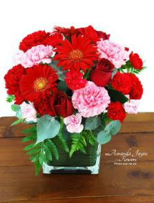 Glass vase arrangement compact with flower of reds and pinks.