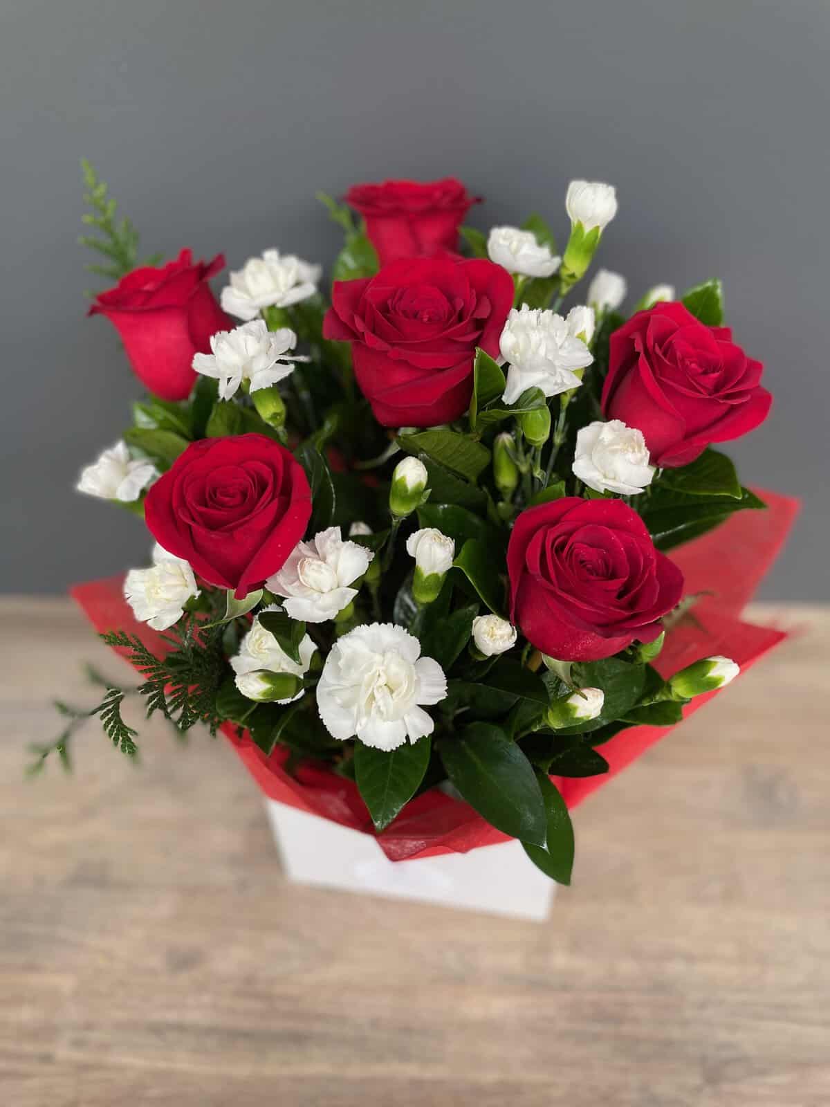 Red long stemmed roses with white carnations presented in a box